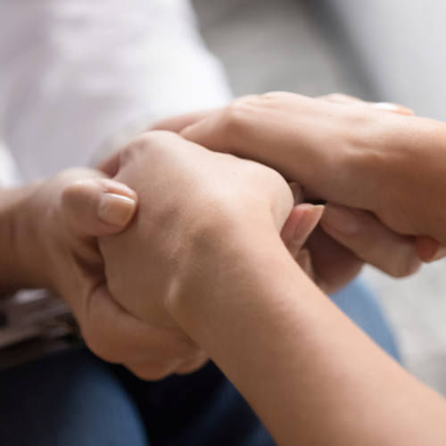 Close up image doctor in white uniform holding hands of female patient, showing support