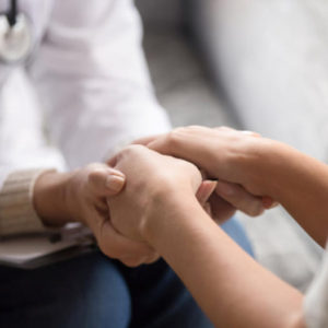 Close up image doctor in white uniform holding hands of female patient, showing support